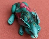 Aquamarine rabbit with dark hibiscus on the back. Polymer clay hand painted miniature by Madre Olius