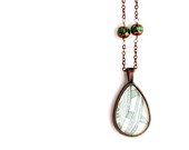 Modern necklace made with vintage sheet music illustration of green leaves under glass set in copper pendant with beads