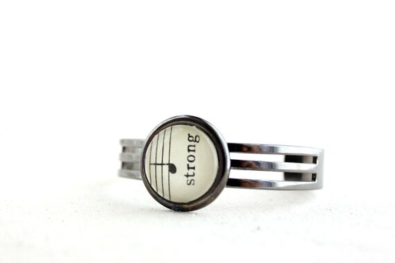 Unisex cuff bracelet for man or woman in shiny gunmetal black adjustable made with vintage sheet music uplifting word strong