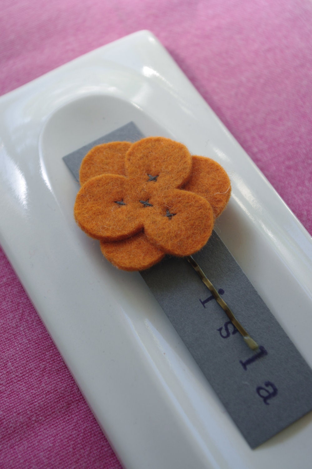 Orange wool felt flower hair clip with brown stitching.