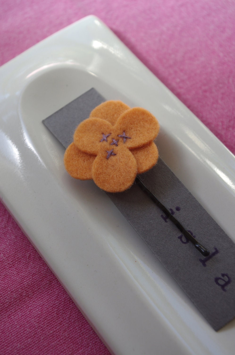 Orange wool felt flower hair clip with brown stitching.