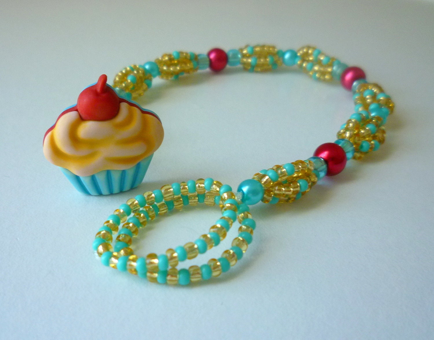Aqua blue, gold, and red beaded bracelet with a beige and light blue cupcake button closure