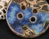 Handmade porcelain button, black graphic against buff background, celestial blue accent glaze. (EB197)