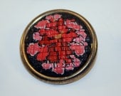 Small brooch in faux needlepoint technique of polymerclay flower design in base metal bezel.