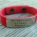 A riveted, 1/2 inch wide red leather cuff bracelet hand stamped with be faithful in small things