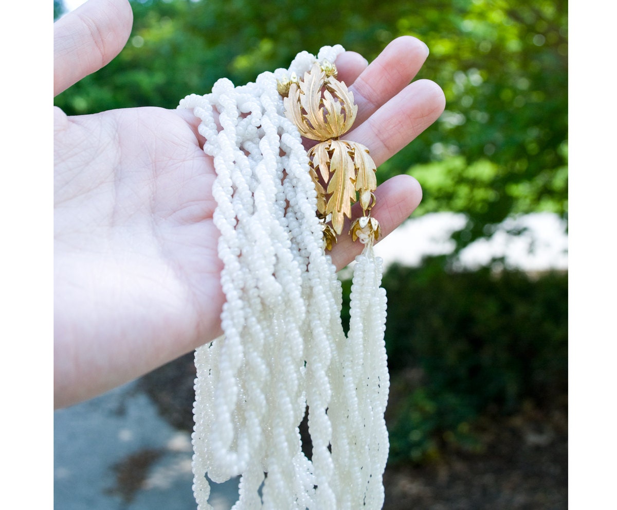 60s - six strand glowing white long necklace with gold tone leaf clasp