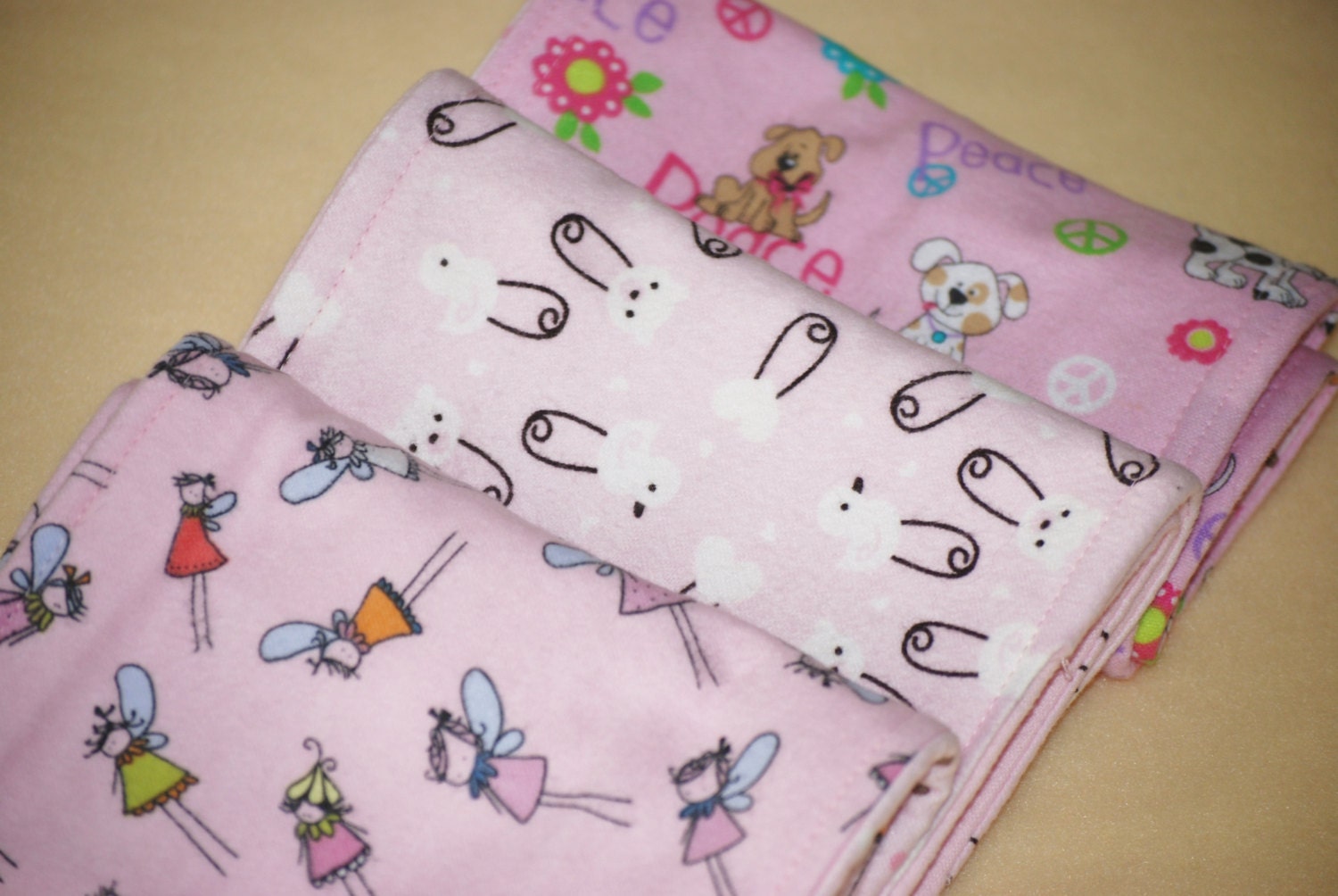 Set of three flannel burp cloths in assorted pink designs (fairies, duck pins, peace pups)