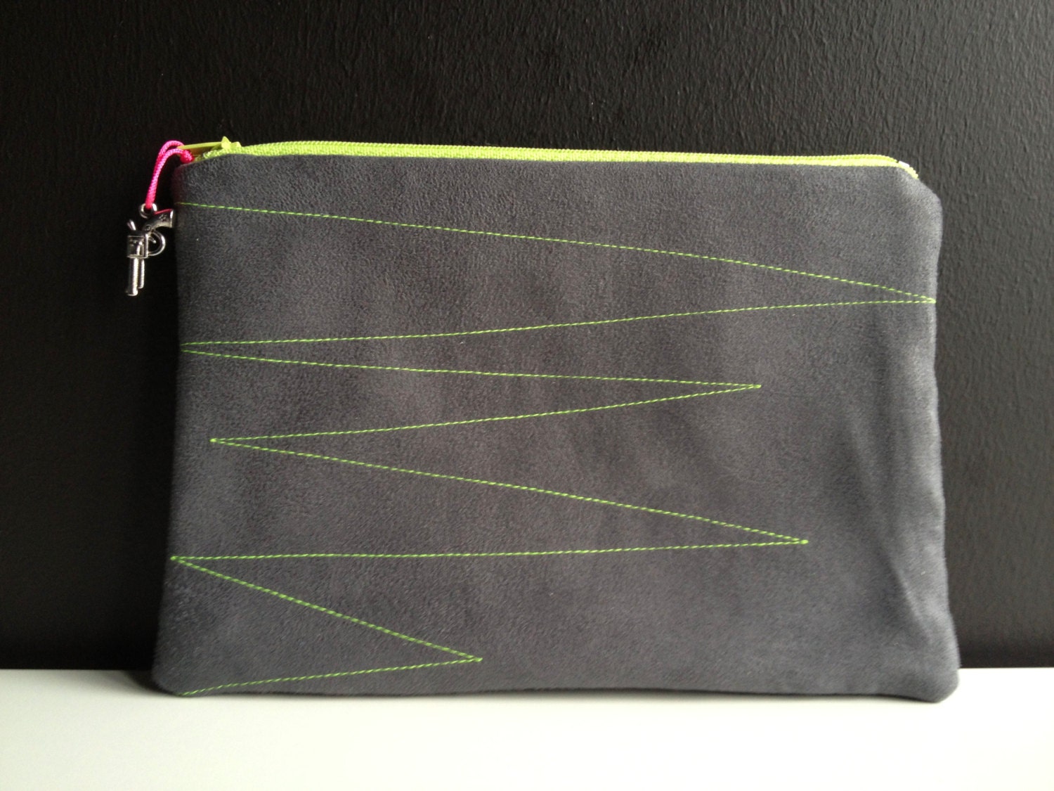 dark grey pouch made of faux leather with stitched geometric lines in neon yellow