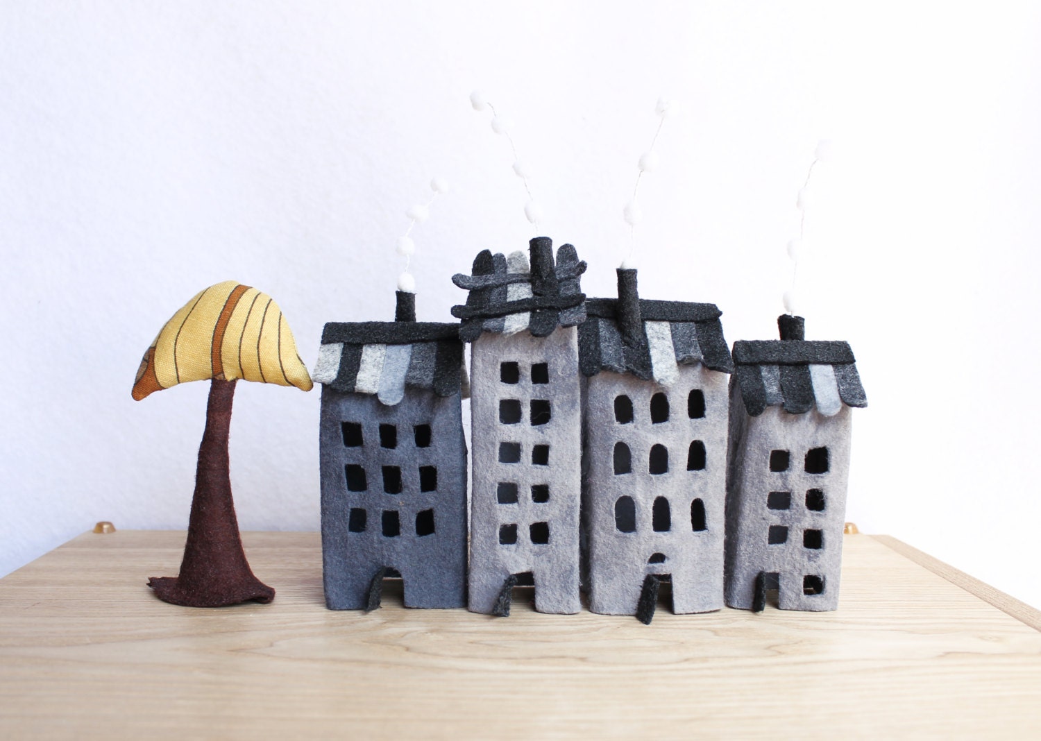 Four grey buildings of felt, with a tree. Miniature. Decoration.