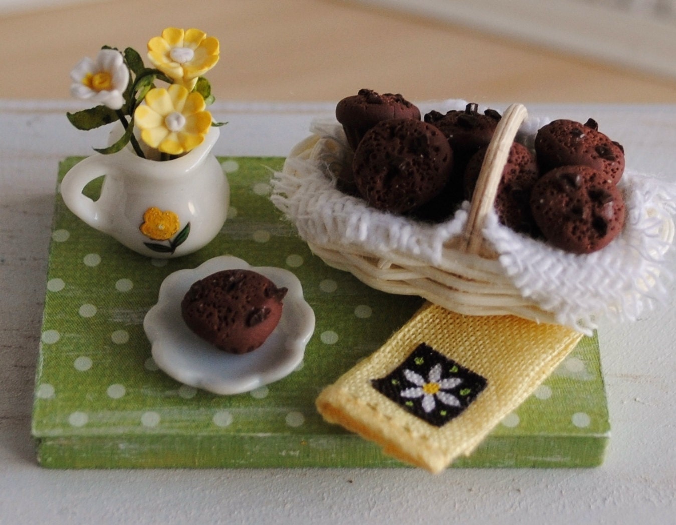 Miniature Basket Of Chocolate Chocolate Chip Muffins, A Pitcher Of Yellow And White Flowers, And A Matching Linen Tea Towel