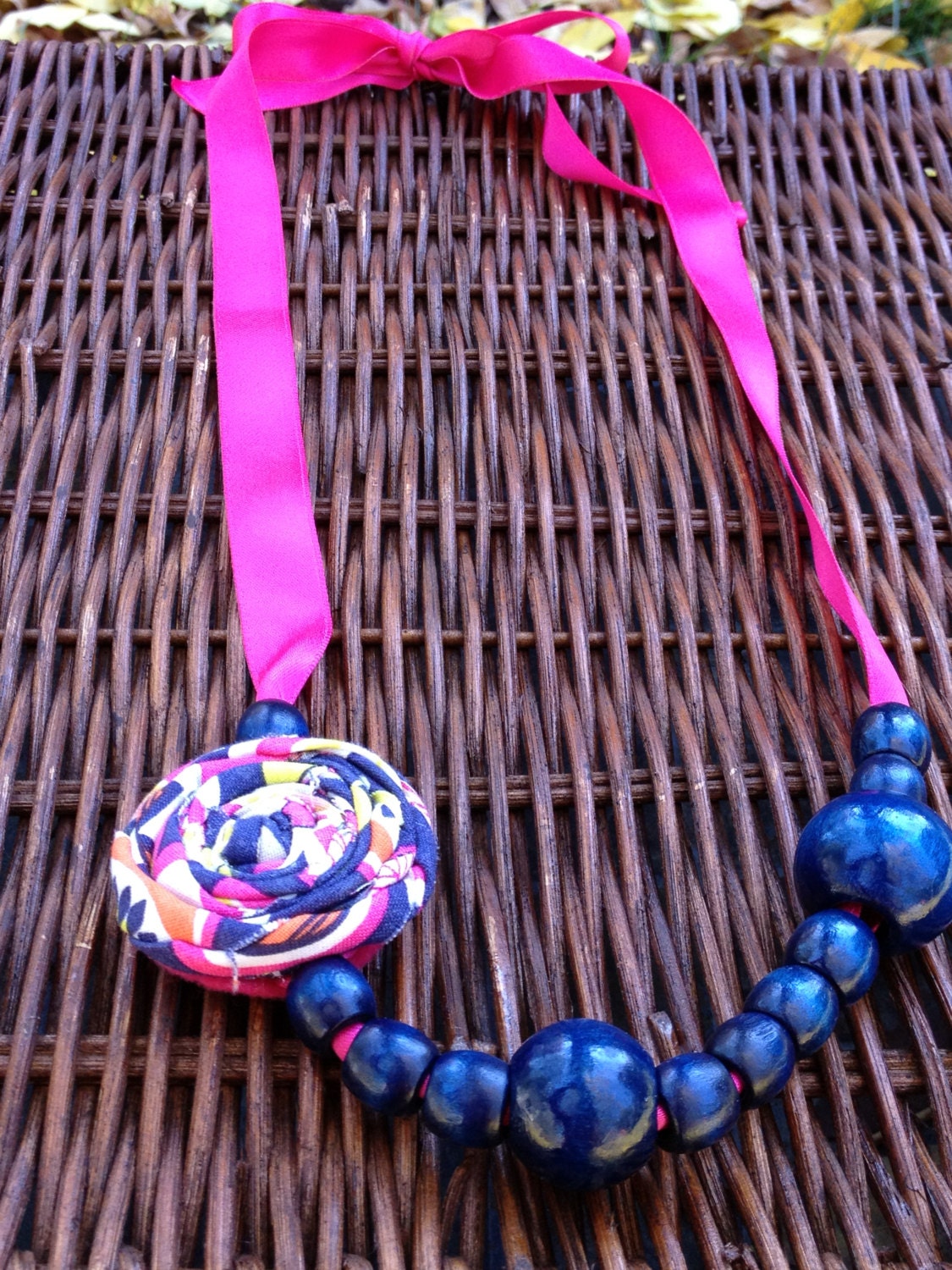 Women's statement necklace with rosette and navy beads on a hot pink ribbon that can be tied to wear short or long